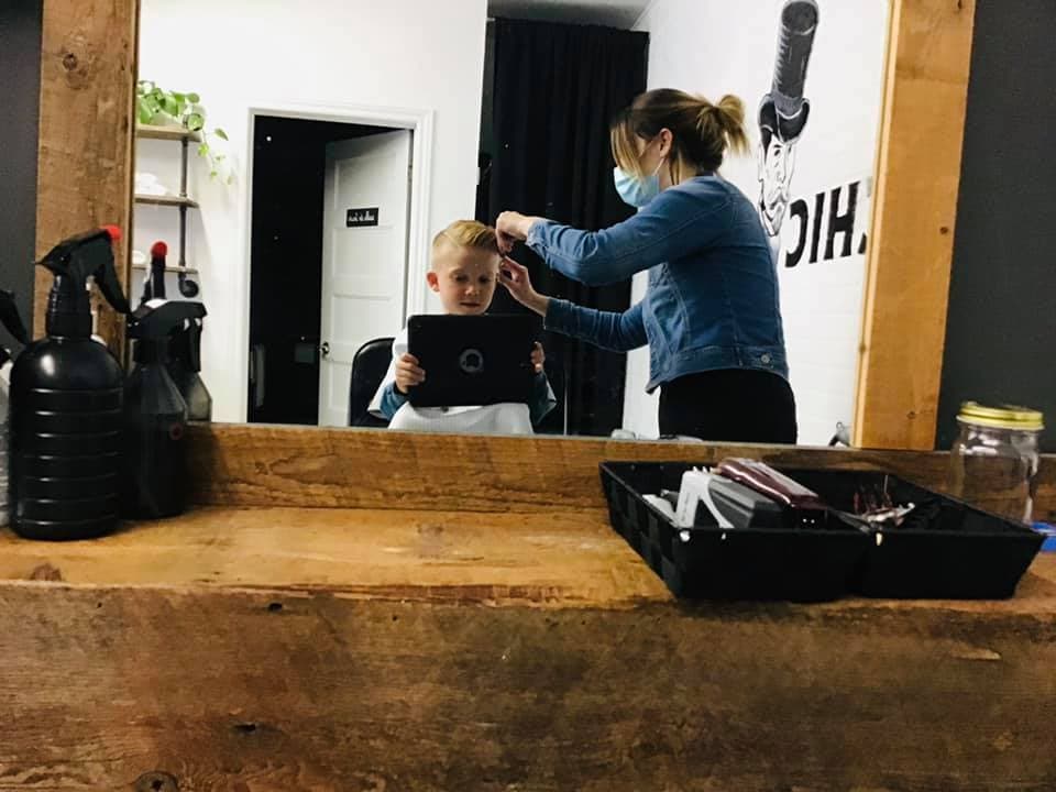 Mélissa coupe les cheveux d'un enfant qui joue sur un Ipad.